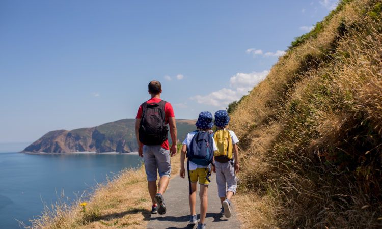 Father and two boys, family walking on a small path along the stunning Devonshire coastline near Lynmouth in Devon, England, UK