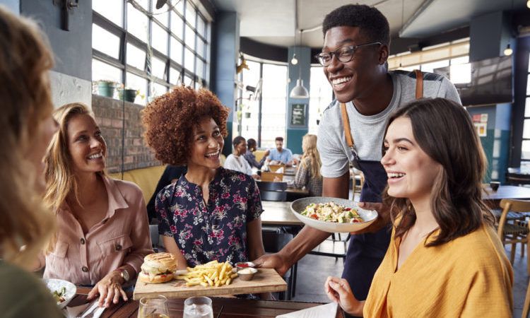 Waiter Serving Group Of Female Friends Meeting For Drinks And Food In Restaurant