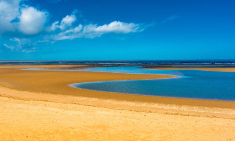 Tide pool of water at low tide on Barnham Overy Staithe beach on Holkham bay, North Norfolk coast, East Anglia, England, UK.