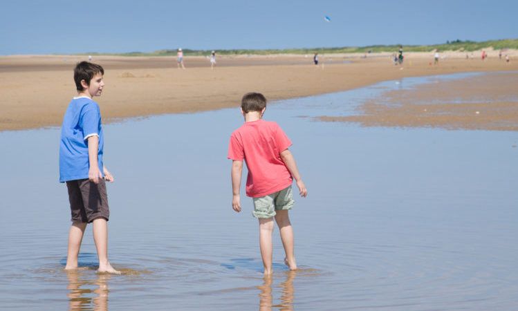 two boys paddling and talking in low tide, Norfolk, UK