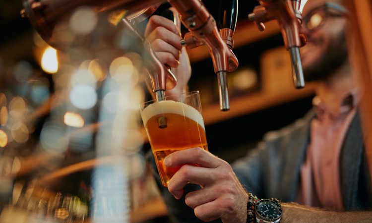 Tattooed barman pouring beer while standing in pub.