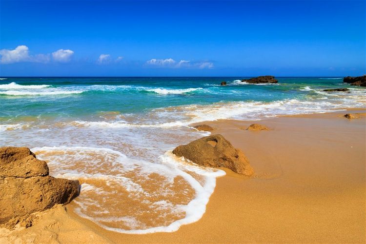 beaches in sardinia | golden sand beach and rocks by blue ocean under clear skies | Spiaggia di Piscinas