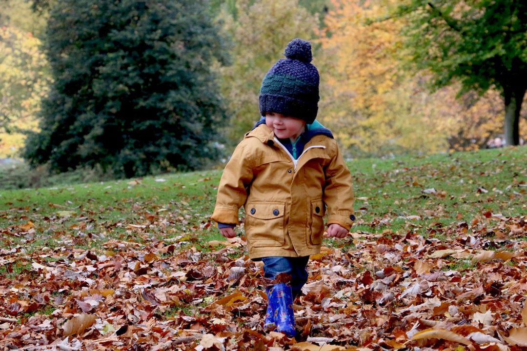 kid playing in leaves with wooly hat on