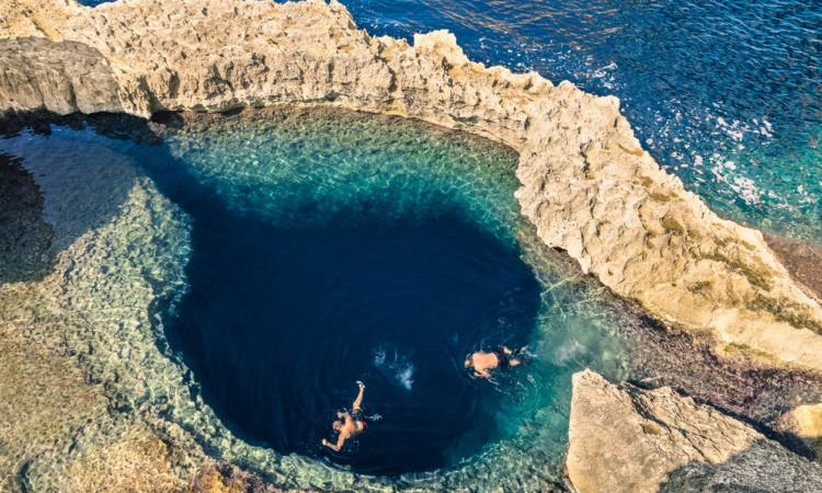 Deep blue hole at the world famous Azure Window in Gozo island - Mediterranean nature wonder in the beautiful Malta - Unrecognizable scuba divers swimming to adventure water cave