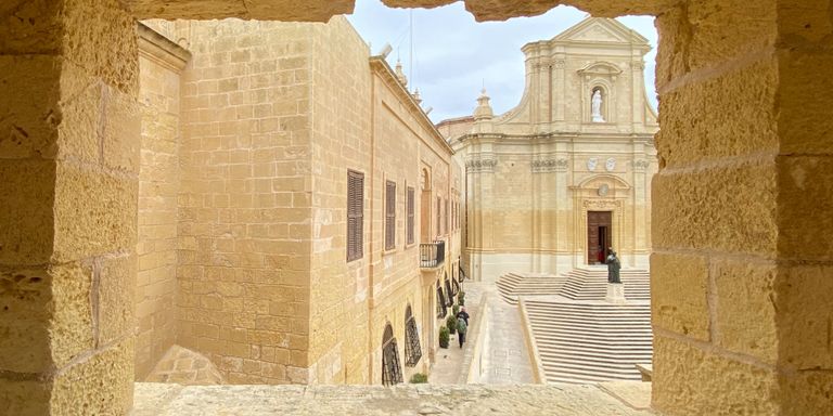 one of the things to do in Gozo: an image of the cathedral through a rocky window