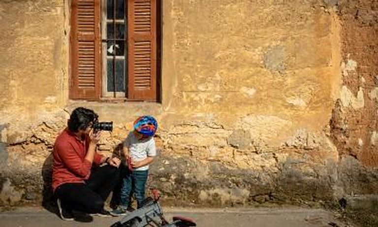 Women taking a photo of young boy, brick house backdrop