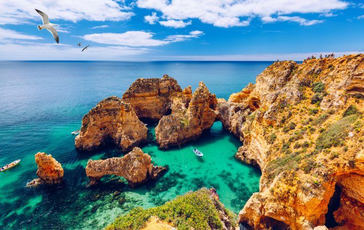Panoramic View, Ponta Da Piedade With Seagulls Flying Over Rocks Near Lagos In Algarve, Portugal. Cliff Rocks, Seagulls And Tourist Boat On Sea At Ponta Da Piedade, Algarve