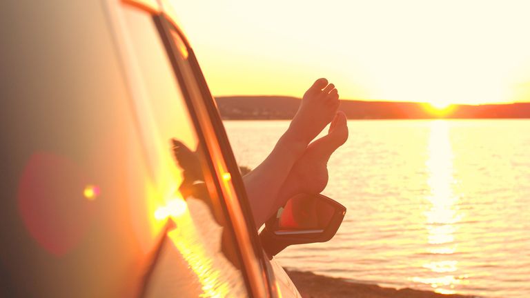 feet hanging out car window at sunset