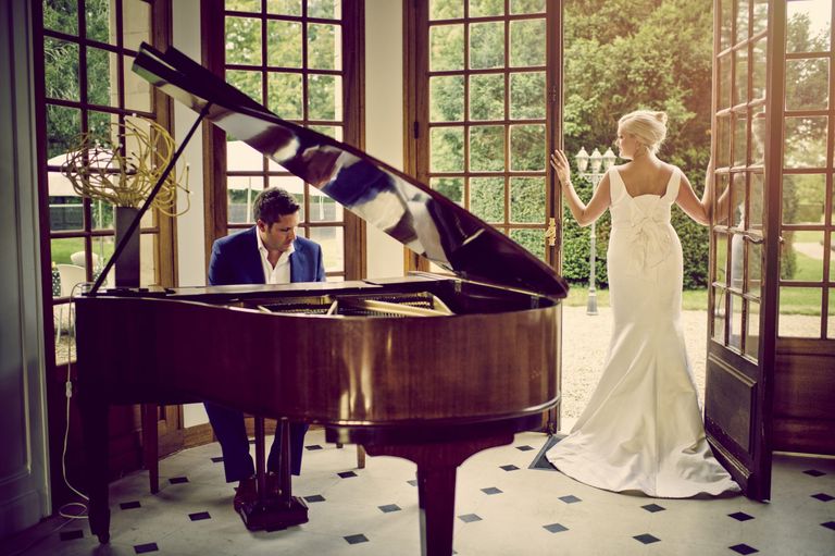 bride looking out glass doors and man playing the piano