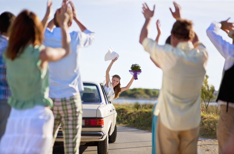 Bride waving to wedding guests from car